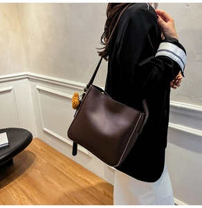Détail du sac seau marron foncé avec breloque ours en peluche et bandoulière en cuir chic