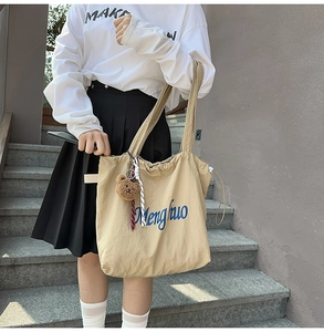 Detail of khaki canvas tote bag with blue artistic lettering and plush bear charm
