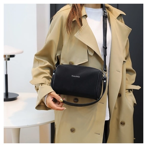 Détail d'un sac cylindrique en cuir noir porté avec un trench-coat élégant et moderne