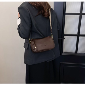 Close-up of brown leather crossbody bag with wide woven strap and side tassel detail