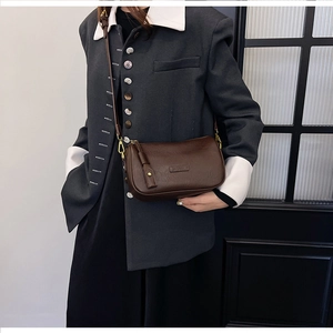 Brown vintage leather shoulder bag with gold buckles worn over a grey blazer