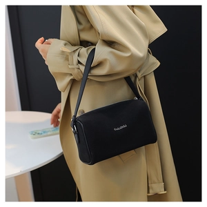 Détail d'un sac polochon en cuir noir porté par une personne en trench-coat beige
