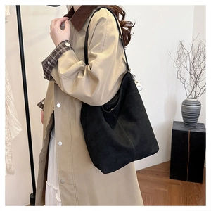 Detail einer großen schwarzen Wildleder-Einkaufstasche mit Baseball-Anhänger am Trenchcoat