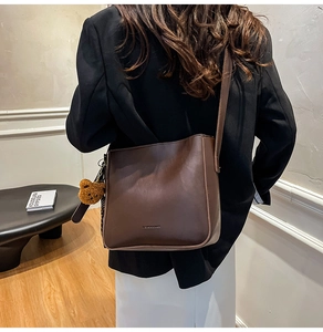 Gros plan d'un sac seau rétro marron foncé avec un charm ours porté par un mannequin