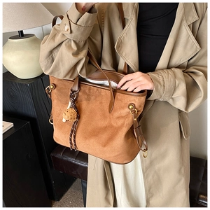 Gros plan d'un sac cabas en daim marron avec garniture en cuir et breloque sur manteau beige