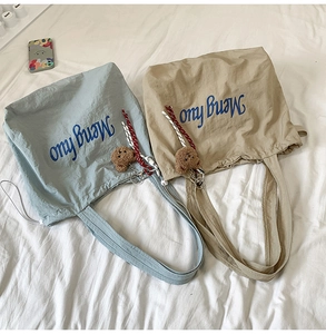 Detail of light blue and khaki nylon tote bags with bear charm and rope decoration