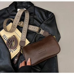 Detail of dark brown vintage texture crossbody bag with wide geometric strap and branding