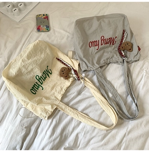 Close-up of canvas tote bag with drawstring closure, plush bear charm and ribbon detail