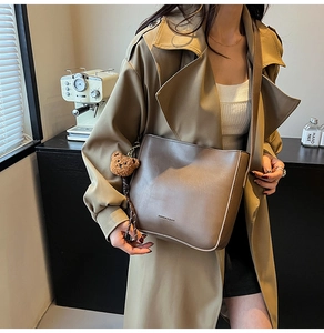 Détail du sac cabas en cuir mat taupe avec breloque ours en peluche et trench-coat