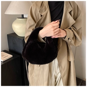 Détail d'un sac croissant noir en peluche avec chaîne argentée porté avec un trench-coat