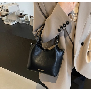 Détail d'un sac à main en cuir noir avec lettrage doré porté par un mannequin