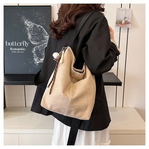 Detailansicht der khakifarbenen Schultertasche mit Baseball-Anhänger und Kontrastnähten