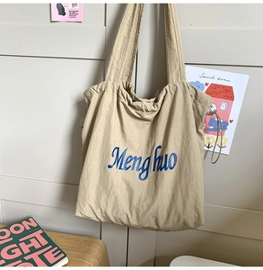 Close-up of beige canvas tote bag featuring blue lettering and side drawstring details