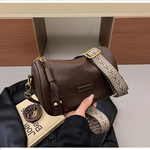 Brown leather cylinder bag with vintage texture and wide geometric pattern strap
