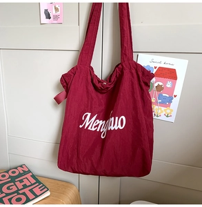 Detail of the deep red textured tote bag with white script lettering hanging on a door