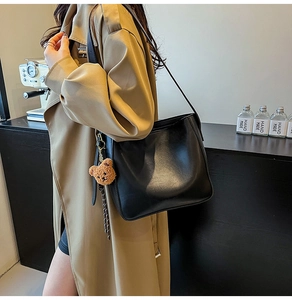 Détail d'un sac sous le bras noir semi-circulaire avec un charmant ours en peluche marron