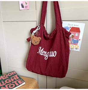Detail of burgundy nylon tote bag with white lettering and plush bear accessory