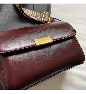 Detail of burgundy leather crossbody bag with vintage gold buckle and woven strap