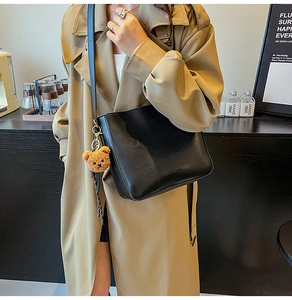Détail d'un sac seau noir en cuir avec un joli pendentif d'ours en peluche marron