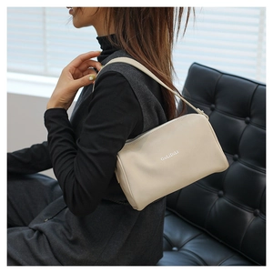 Gros plan du sac oreiller en cuir crème avec fermeture éclair et détail du logo