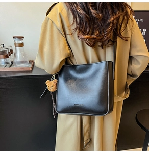 Détail d'un sac seau noir avec un charm ours en peluche porté avec un trench élégant