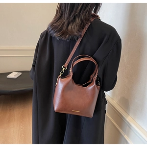 Sac seau en cuir marron porté à l'épaule par un mannequin avec finition mate élégante