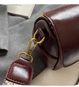 Close-up of glossy burgundy leather bag with gold hardware and woven strap detail