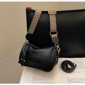 Close-up of black crossbody bag with geometric wide strap and gold hardware on magazines