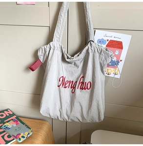 Macro view of light grey nylon tote bag showing red script logo and drawstring detail
