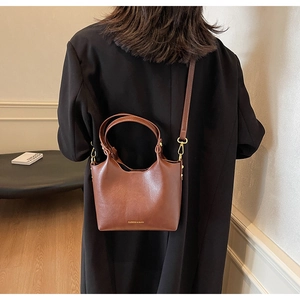 Sac seau bandoulière en cuir marron porté avec un manteau noir pour un style élégant