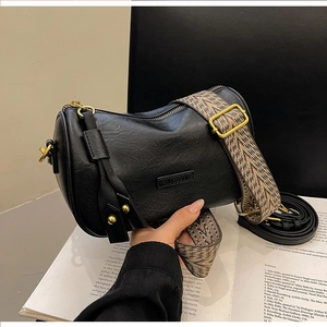Detailed macro view of black textured leather pillow bag with wide patterned shoulder strap