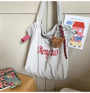 Macro shot of grey fabric tote bag featuring red text embroidery and plush bear charm
