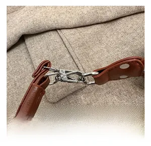 Détail macro du fermoir mousqueton argenté et bandoulière en cuir sur tissu à chevrons