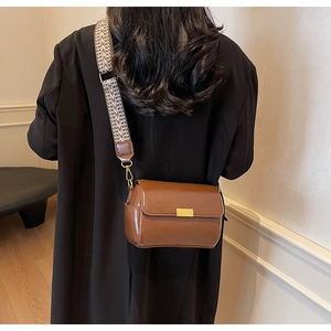 Detail of a brown leather crossbody bag featuring a wide woven herringbone strap and gold lock