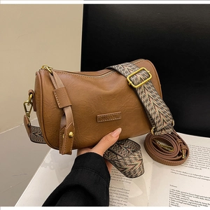 Detail of MUCOOU brown cylinder bag showing wide bohemian strap and leather texture