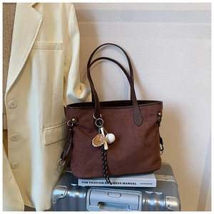 Détail du sac cabas en daim avec poignées en cuir et breloque baseball sur une valise