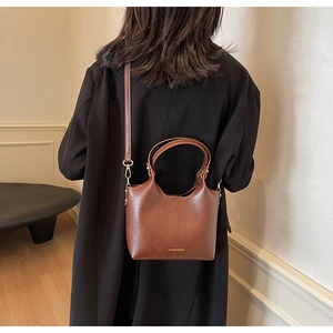 Détail du sac seau en cuir marron avec accessoires dorés et bandoulière amovible