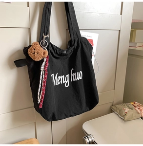 Detail of a large black tote bag with white text and a cute brown bear plush charm