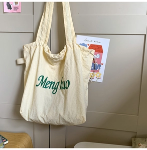Close-up of cream tote bag featuring green script print and adjustable side drawstrings
