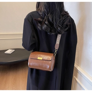 Detail view of a vintage dark brown shoulder bag with a wide jacquard woven strap on black coat