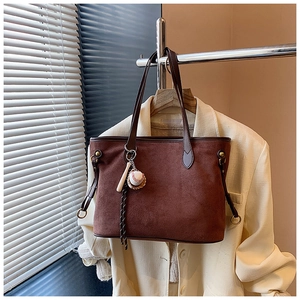 Détail du sac cabas en daim marron avec pendentif de baseball sur un cintre en métal