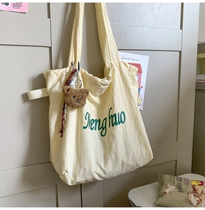 Detail of beige tote bag with green Shenghuo print and cute brown plush bear charm