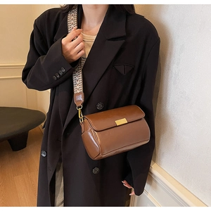 Close-up of brown leather crossbody bag with geometric woven strap and gold buckle