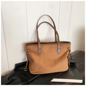 Détail d'un sac cabas en daim marron avec anses en cuir et anneaux métalliques dorés