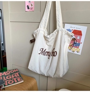 Detail of beige tote bag with brown Mengho print and drawstring side on a closet door