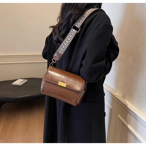 Close-up of retro brown oil-wax leather pillow bag with wide geometric woven strap