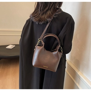 Gros plan d'un sac seau marron foncé avec détails dorés porté sur un manteau en laine