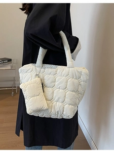 White quilted tote bag with matching pouch shown on a shoulder in minimalist indoor setting