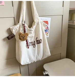 Detail of off-white canvas tote bag featuring brown artistic text and plush bear charm
