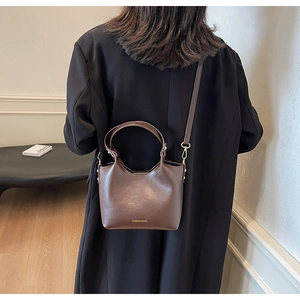 Détail d'un sac seau en cuir mat marron foncé avec poignées et lettrage du logo